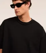 Remera negra de algodón con corte oversized, cuello redondo y manga corta. Presenta un tejido acanalado y un dobladillo sin rematar.