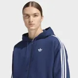 Campera con capucha Adidas Adicolor de corte holgado, color azul con cierre frontal de cremallera. Presenta las icónicas tres rayas blancas en las mangas y el logo del trébol bordado en el pecho.