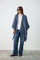 Ruana de tejido de punto grueso en color azul jean, con diseño abierto y terminaciones con flecos en el ruedo.