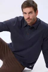 Remera polo de manga larga confeccionada en tejido jersey, con cuello clásico y cierre frontal de tres botones. Presenta un diseño liso con un pequeño logo bordado en el pecho y una etiqueta decorativa en el ruedo.