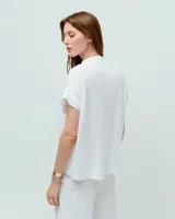 Remera blanca de lino con cuello mao, media cartera con broches metálicos y manga japonesa. Presenta un bolsillo frontal tipo plaqué, recortes laterales en sisa con detalles de encaje y ruedo redondeado con corte escalonado.