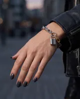Pulsera de eslabones gruesos en acero plateado, combinada con un eslabón en baño de oro y un dije central en forma de candado plateado.