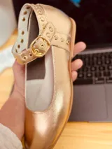 Zapato tipo Mary Jane dorado de cuero, con correa con hebilla y tachas.