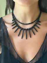 Collar doble de estilo tribal en color negro. La primera capa es una gargantilla de cuentas pequeñas y la segunda capa es un collar con bastones de piedras reconstituidas y cuentas redondas. Se cierra con cadena de acero quirúrgico.
