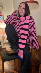 Bufanda de tejido de punto con diseño de rayas horizontales en color rosa y negro, con un detalle de bloque de color azul en uno de los extremos.