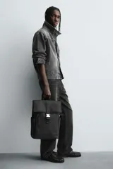 Mochila negra con acabado engomado, solapa con hebilla de liberación rápida, compartimento principal con espacio para dispositivos de hasta 13 pulgadas y bolsillo con cremallera, bolsillo frontal con cremallera, parte posterior acolchada con banda de sujeción para equipaje, asa de mano y dos asas de hombro ajustables y acolchadas.