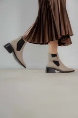 Botineta de cuero charol negro con acabado brillante, diseño de punta fina y taco cuadrado. Presenta un panel elástico lateral y una correa decorativa con hebilla metálica plateada.