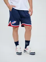 Short deportivo Umbro del Club Nacional de Football, modelo Match para hombre. Diseño en color azul marino con tejido de malla, detalles en blanco y rojo en los laterales y el escudo del club bordado.