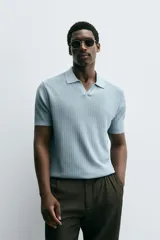 Polo de manga corta, color celeste pálido, con cuello solapa y abertura frontal en V. Tejido de punto con textura acanalada vertical.