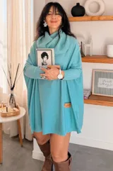 Polerón oversize de tejido de punto en color turquesa, con cuello polera amplio, mangas largas con puños acanalados y corte holgado. Presenta un detalle de etiqueta de cuero en el frente.