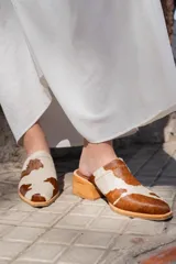 Zuecos con base de madera y capellada de cuero con estampado animal en tonos marrones y blancos.