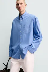 Camisa de corte regular fit confeccionada en tejido de algodón de color azul. Cuenta con cuello solapa, manga larga con puño abotonado, bolsillo de parche en el pecho y cierre frontal con botones.