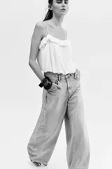Jean de cinco bolsillos en denim de algodón rígido, corte holgado con cierre y botón. Cuenta con piernas amplias de diseño curvado, raya marcada y bajo deshilachado.
