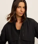 Campera deportiva cortaviento color blanco, con capucha ajustable, cierre frontal por cremallera y diseño de corte holgado. Incluye saquito para guardar.