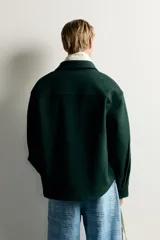 Sobrecamisa de ajuste relajado en color azul marino, con cuello de solapa, manga larga con puño abotonado y cierre frontal con botones. Presenta bordados contrastantes en el frente con la inscripción "St. Louis Worldwide Goods" en tonos naranja y blanco.