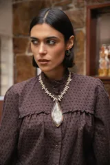 Collar corto con dije central en forma de hoja, elaborado en guampa con engarce de alpaca. La cadena está compuesta por bastoncitos de acrílico y mostacillas transparentes, finalizando con una cadena de eslabones de acero quirúrgico ajustable.