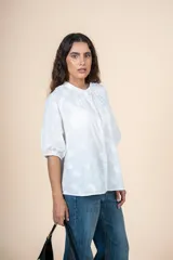 Blusa de algodón color blanco con bordado sutil en relieve, cuello redondo, cierre frontal con botones y mangas tres cuartos con terminación elástica.