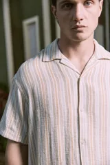 Camisa de manga corta con fit relajado y cuello resort. Cierre con botones al frente y diseño a rayas verticales en tonos beige, blanco y naranja. Confeccionada en tejido plano de algodón y algodón orgánico, estilo liviano ideal para el verano.
