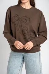Sweater marrón de algodón con cuello redondo y diseño de moños en relieve bordados en el frente.