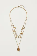 Collar doble dorado con dijes de conchas marinas, cuentas y piedra colgante.