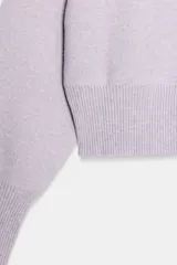 Chaqueta corta de punto color lila, con cuello redondo, manga larga con puños acanalados y cierre frontal con botones negros. Presenta un diseño con acabado en rib en el ruedo.