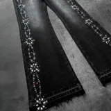Pantalón de jean negro de corte flared con efecto desgastado, tiro medio y detalles de pedrería y tachas formando patrones en los laterales de las piernas.