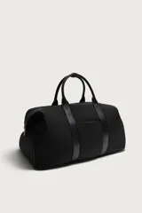 Bolso de viaje tipo bowling fabricado en combinación de nylon y detalles en cuero sintético, de color negro. Cuenta con compartimento principal con cierre de cremallera, bolsillo frontal plano, dos asas de mano y un asa de hombro ajustable y extraíble.