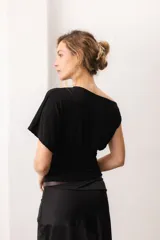 Top negro de manga corta ancha y escote bote con caída asimétrica en los hombros. Presenta un diseño ajustado en la cintura con frunces laterales.