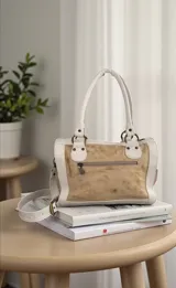 Cartera de cuero natural de diseño contemporáneo y versátil, intervenida con arte original por Carolina De Cunto en el frente, combinando tonos marfil y arena con detalles pintados a mano. Cuenta con estructura firme, herrajes de metal, manijas superiores, correa regulable desmontable y bolsillos internos y externos.