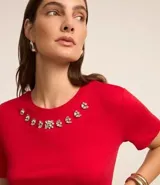 Blusa de manga corta confeccionada en viscosa, con cuello redondo decorado con apliques de cristales en forma de flores. Presenta un diseño femenino y versátil.