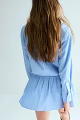 Vestido camisero corto de popelina de algodón en color celeste, con cuello clásico, cierre frontal con botones, mangas largas con puños sencillos y cordón ajustable en la cintura.