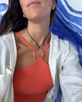 Collar con dije colgante de forma orgánica e irregular, acabado dorado, suspendido de un cordón negro de algodón natural.