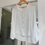 Camisa de lino blanca con mangas largas abullonadas, puños elásticos y cuello mao con escote en V y botones frontales.