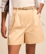 Short de sastrería color beige, de corte recto con pinzas delanteras y trabillas en la cintura. Incluye un cinturón de poliuretano a tono con hebilla metálica dorada.
