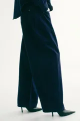 Jean de denim rígido azul oscuro, con corte holgado y diseño curvo en las piernas. Presenta cintura estándar con cordón ajustable, cierre con botón y bolsillos clásicos.