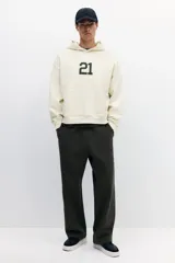 Canguro de algodón pesado color beige, con capucha de doble capa, hombros caídos y bolsillo canguro. Puños y bajo en punto acanalado. Estampado frontal con el número "21" en color negro.