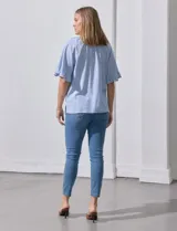 Blusa celeste y blanca a rayas verticales, de lino y corte holgado. Tiene cuello redondo con escote en V y lazo de ajuste. Las mangas son cortas y amplias, con volados en el borde.