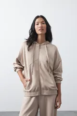 Campera con capucha y cierre frontal, de silueta relajada, hombros caídos y bolsillos laterales. Presenta terminaciones elastizadas en puños y ruedo, con líneas de recorte frontales y cierre metálico con tirador circular.