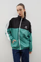 Campera de tela avión con diseño color block en negro y verde, con detalles de franjas blancas en las mangas. Presenta cierre frontal completo, cuello alto, puños y ruedo elásticos, y logo bordado en el pecho.