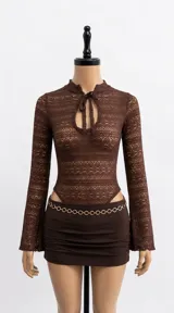 Body negro confeccionado en encaje transparente, con mangas largas acampanadas, cuello alto y abertura frontal con lazo para atar.