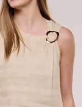 Blusa sin mangas de lino color beige, de calce recto y escote asimétrico con detalle de hebilla metálica decorativa y pliegue fruncido en el hombro.