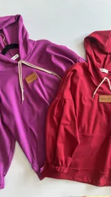 Canguro con capucha y cordones ajustables, confeccionado en tejido de punto. Presenta mangas largas abullonadas con puños elásticos y un parche de cuero sintético con logo en el pecho.