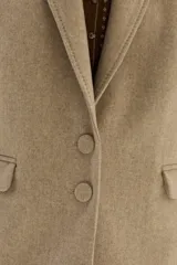 Blazer de paño color beige, con solapas clásicas y bordados decorativos en tono más oscuro en la parte inferior de las mangas.