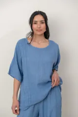 Blusa de lino color marrón oscuro, con escote redondo, mangas cortas amplias y detalle de alforzas verticales en el lateral derecho.