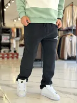 Pantalón de jogging oversize negro con felpa, de corte recto y cordón ajustable en la cintura. Presenta un pequeño estampado de texto blanco en el lateral izquierdo.