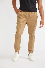 Pantalón cargo color beige de corte slim, con cintura elástica y cordón ajustable. Presenta bolsillos laterales con solapa y velcro, y puños elásticos en los tobillos.