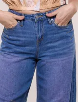 Jean wide leg cropped de tiro medio-alto, confeccionado en denim azul intermedio con efecto degradé y costuras en tono camel. Presenta cinco bolsillos, cierre frontal con botón y cierre, nervaduras decorativas en la zona de las rodillas y ruedo desflecado.