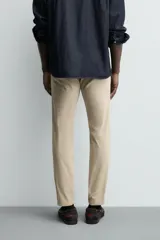 Pantalón chino de corte ajustado, color beige, con bolsillos laterales y bolsillos traseros de vivo. Cuenta con cierre frontal de cremallera y botón.