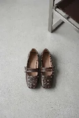 Chatita estilo bailarina color off-white, confeccionada en cuero. Presenta un diseño con doble tira ajustable con hebillas metálicas en el empeine y detalle de cordones cruzados con lazo en la puntera cuadrada. Cuenta con ojales metálicos decorativos en los laterales.