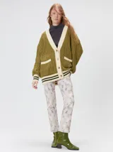 Cardigan de punto trenzado en color negro con detalles en color crema en los bolsillos, puños y ruedo. Presenta un diseño oversize, cierre frontal con botones y bordado decorativo en uno de los bolsillos delanteros.